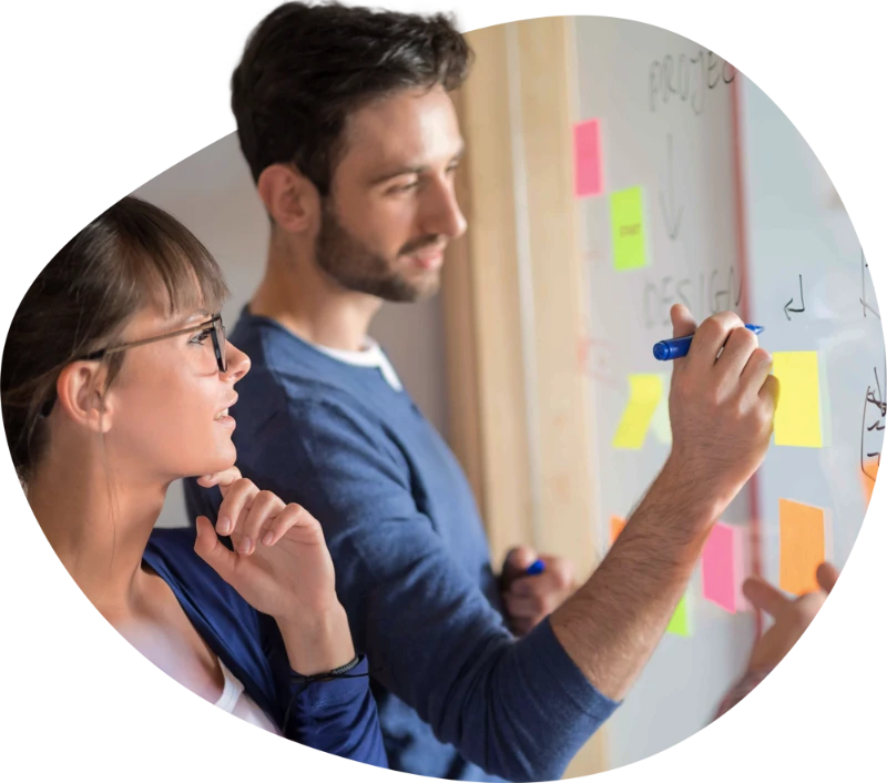 A man and a woman doing a design discussion. Writing on a window and post-its using whiteboard markers.